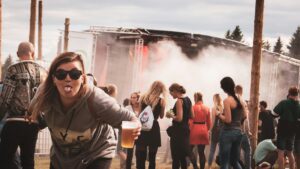 Man in sunglasses drinking a beer on tap in front of a stage at a music festival