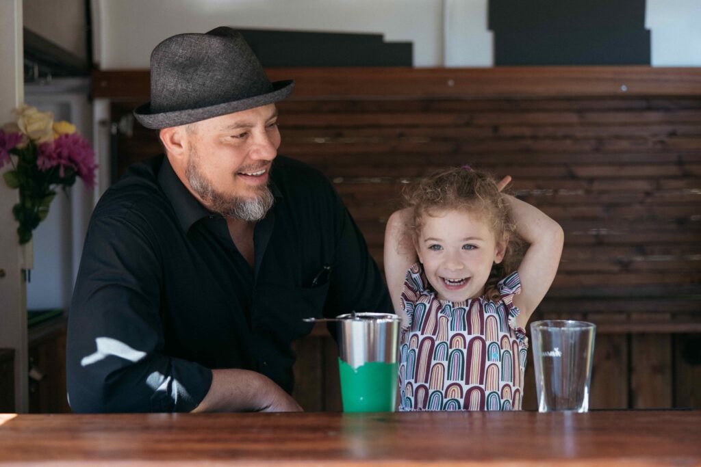 Man and child smiling behind a bar with empty glasses in front of them